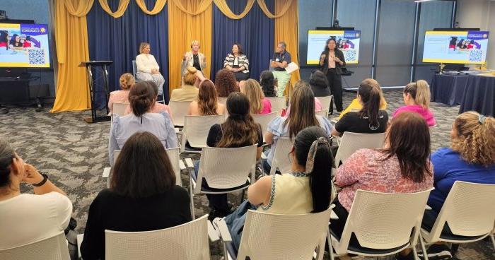 Audience faces a group of five panelists seated at the front of a conference room.