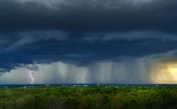 Landscape shows storm clouds overhead with rain coming down in sheets on green landscape.